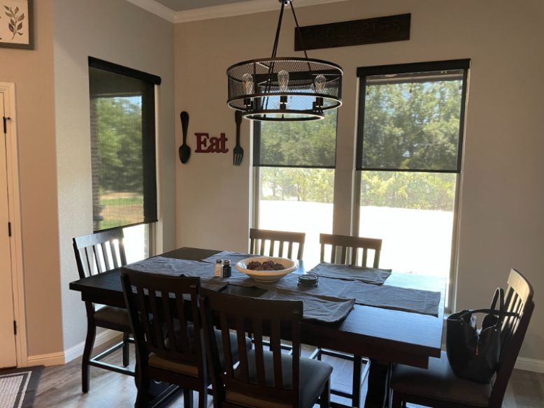 Love is Blinds GA: A dining room with a table and chairs and dark roller shades on three windows.