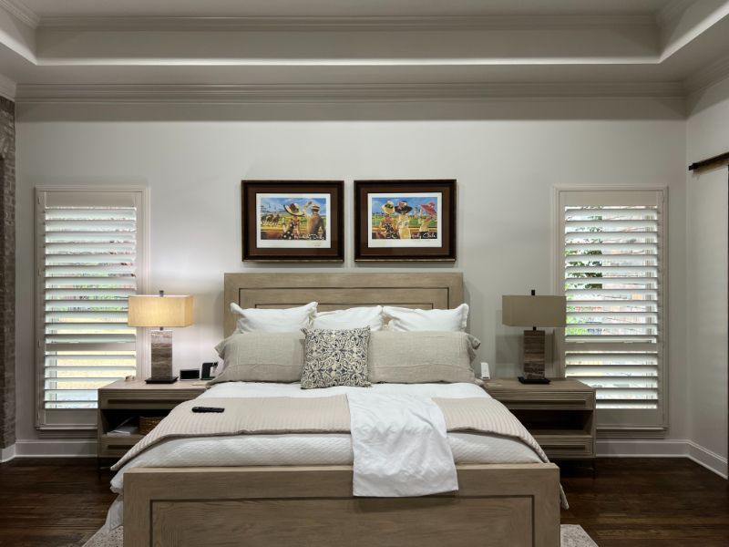 a bedroom with a bed , two nightstands , two lamps and two pictures on the wall custom plantation shutters Love is Blinds Georgia.