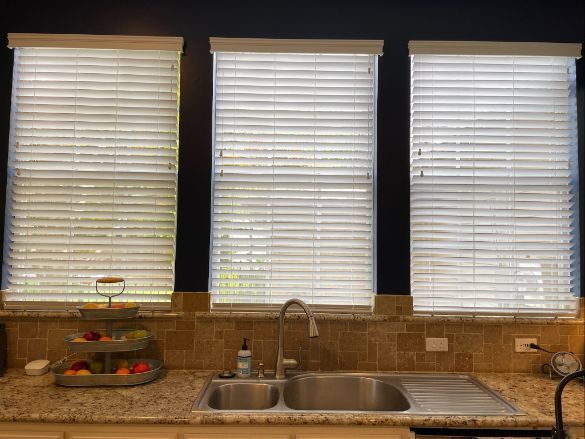A kitchen with a sink and three windows with blinds.