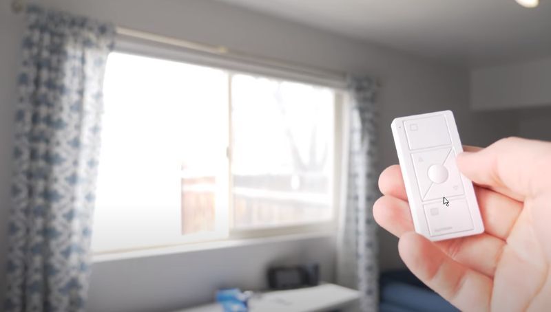 A person is holding a remote control in front of a window in a living room.