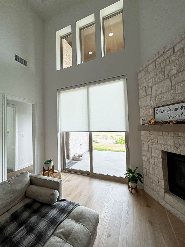 A living room with vaulted ceilings, a fireplace, and patio doors with shades. 