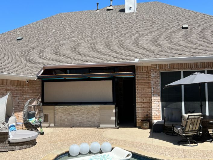 An outdoor pool area has an outdoor kitchen sectioned off by exterior patio shades. 