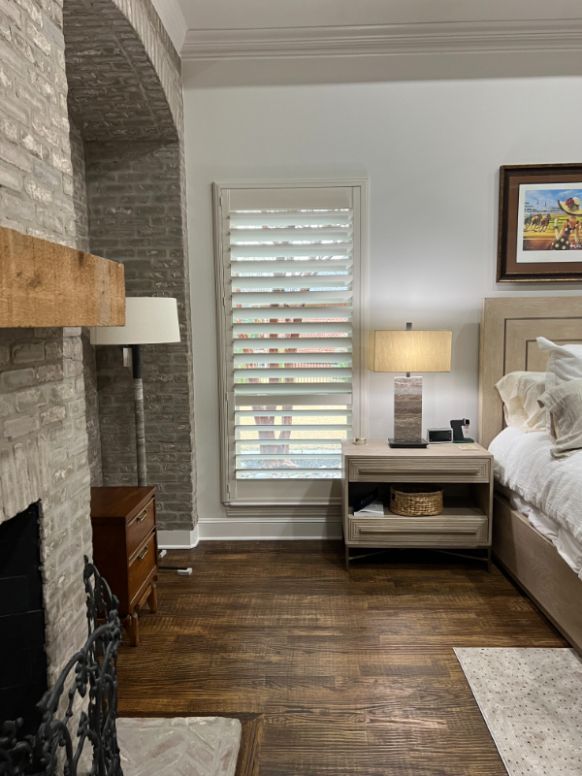 Love is Blinds GA: A bedroom with a bed , nightstand , lamp and fireplace, with shutters on the window.