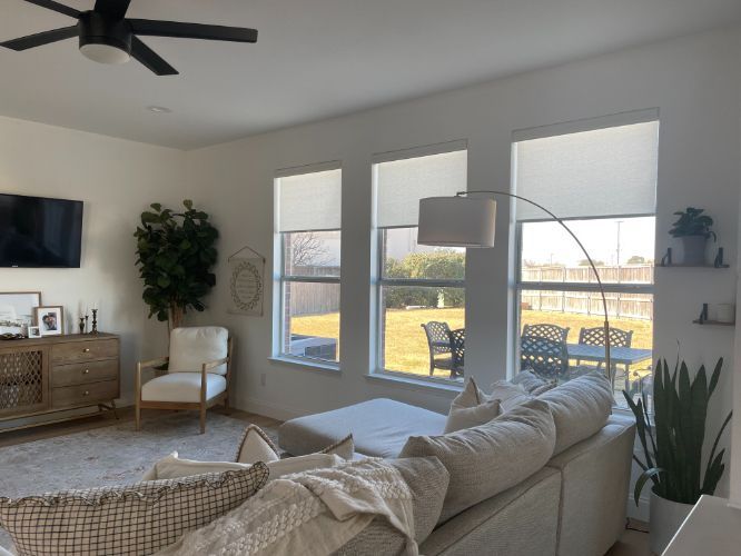 A living room with a couch and chairs and a ceiling fan, cordless shades on the windows.