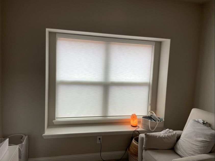 A room with a chair and a window with white cordless blinds.
