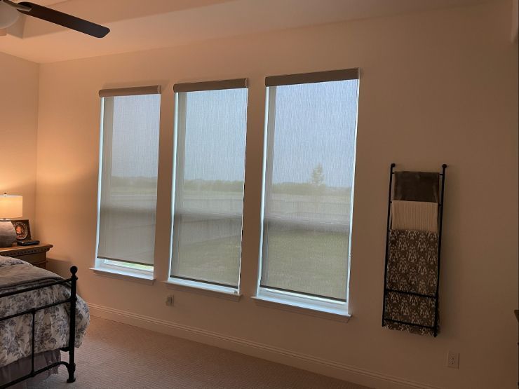 A row of windows in a bedroom has solar shades half-lowered. 