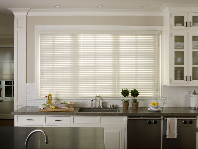 A kitchen has a large window over the sink with honeycomb shades. 