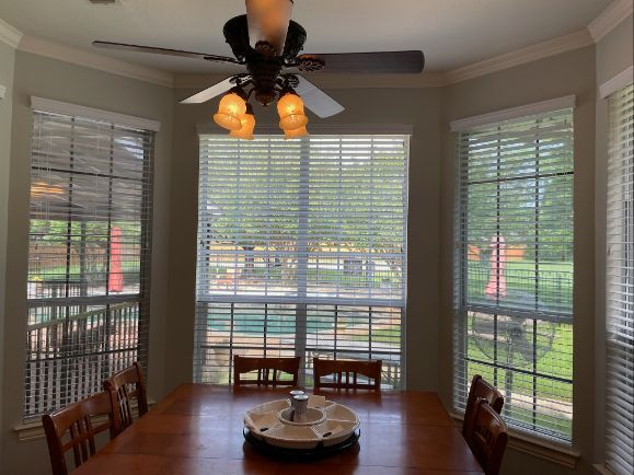 A dining room with a ceiling fan has several windows with wood blinds. 