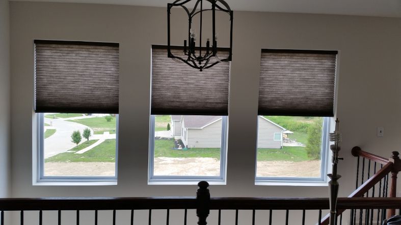 A stairway has three windows with cellular shades. 