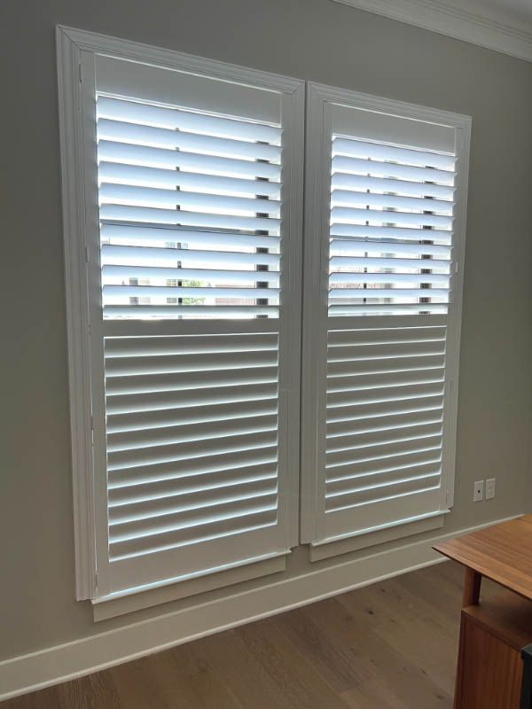 A room with two windows with white shutters on them.