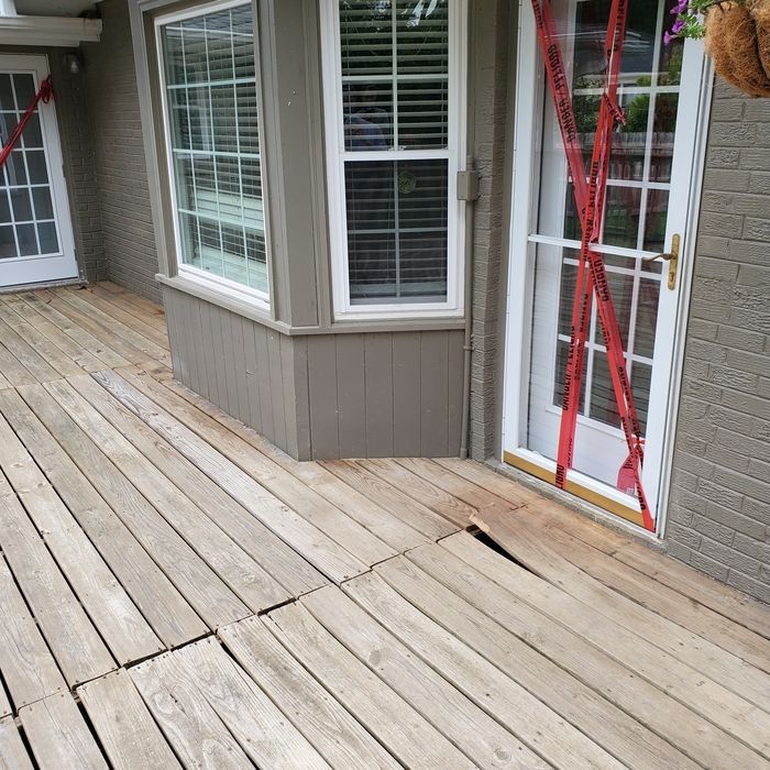 Damaged wooden deck with a doorway blocked by red caution tape. Gray siding and white windows are nearby.
