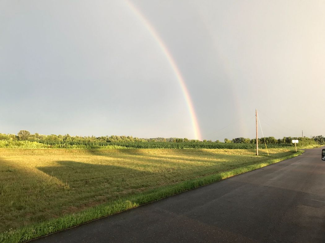 A car is driving down a road with a rainbow in the sky.