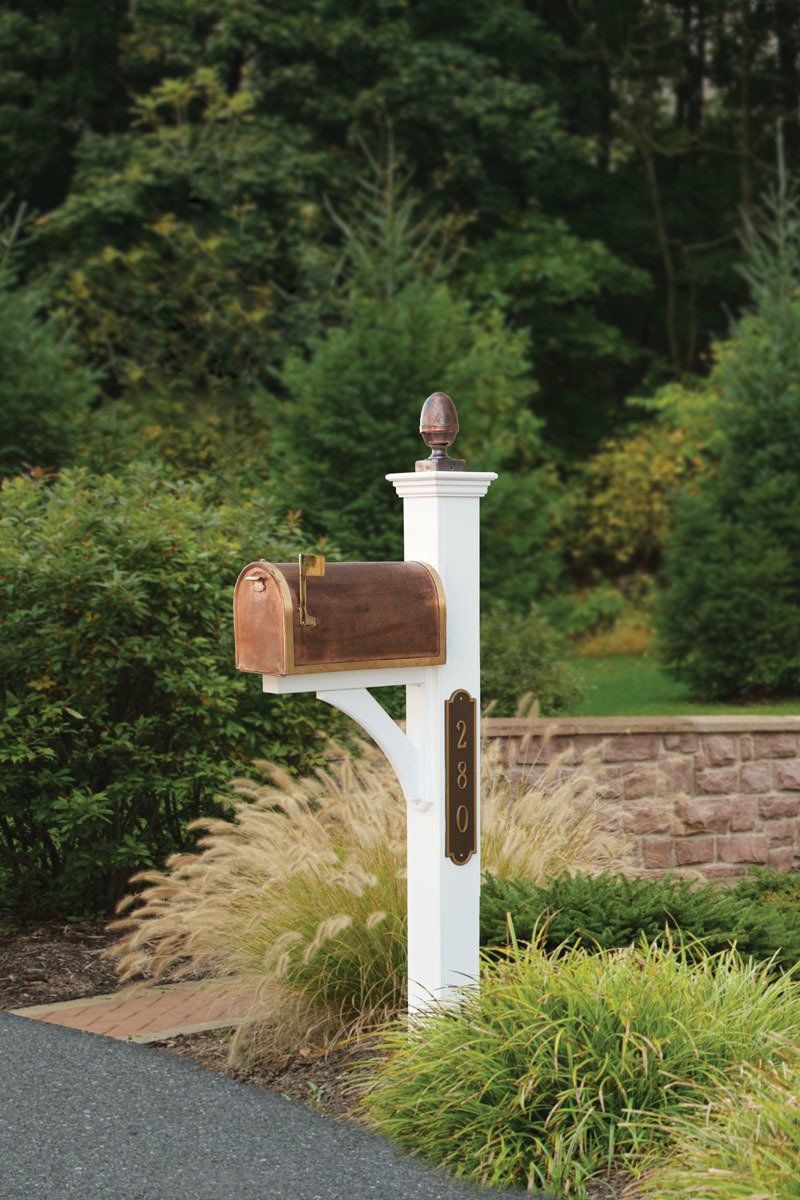 A white mailbox with a brown mailbox is sitting next to a brick wall.