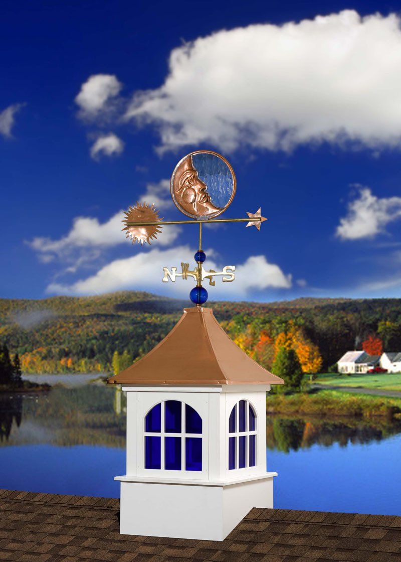 A weather vane on top of a white building with a lake in the background