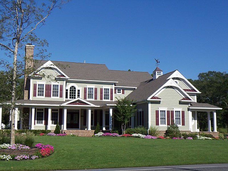 A large white house with red shutters sits on a lush green lawn