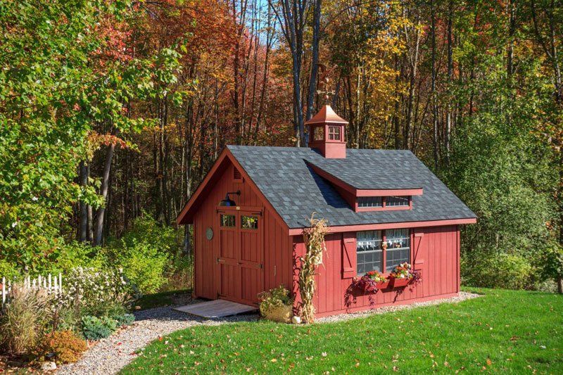 A red shed with a black roof is sitting in the middle of a lush green field.