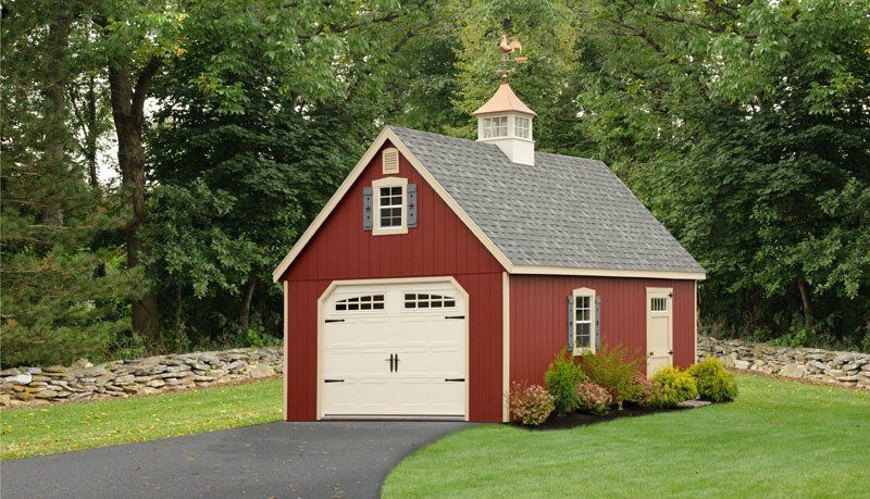 A red garage with a white door is sitting in the middle of a lush green field.