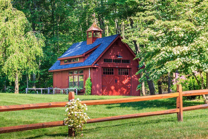 A red barn with a blue roof is behind a wooden fence.