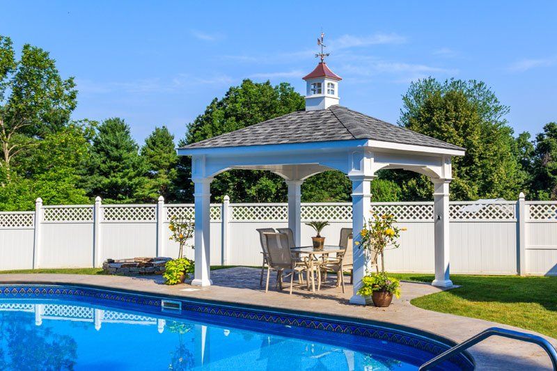 A gazebo with a table and chairs next to a swimming pool.