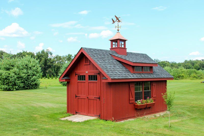 A red shed with a weather vane on top of it is in the middle of a grassy field.