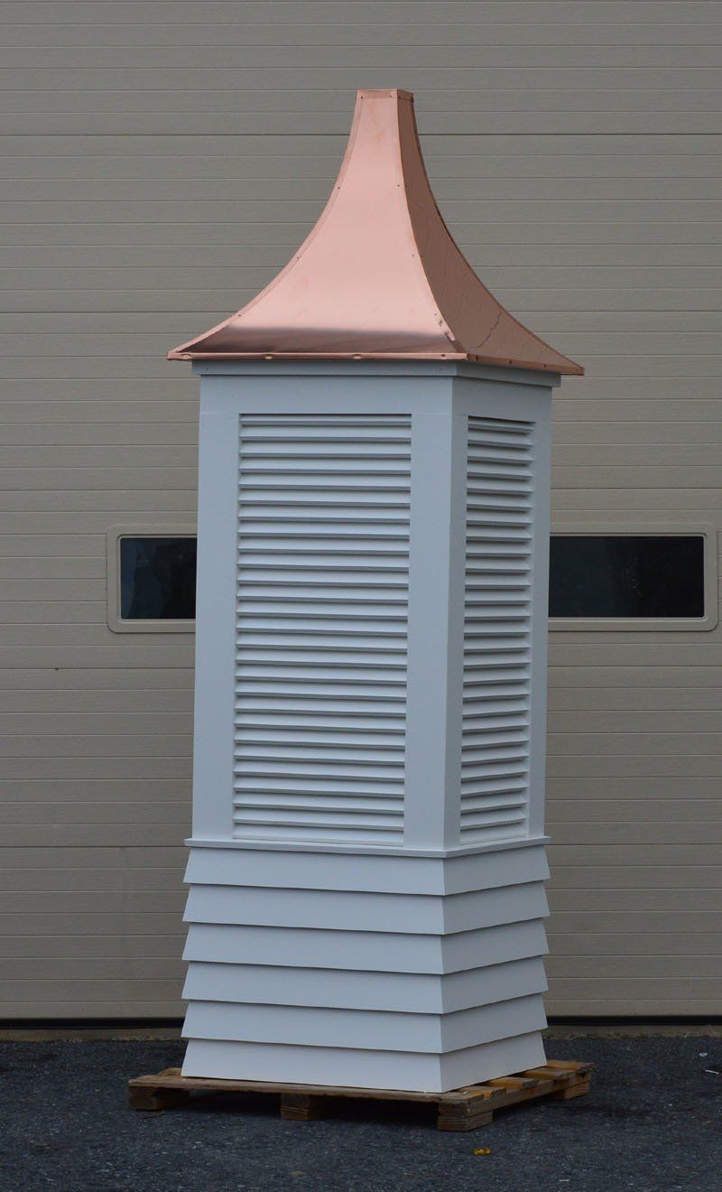 A white building with a copper roof is sitting on a pallet in front of a garage door.