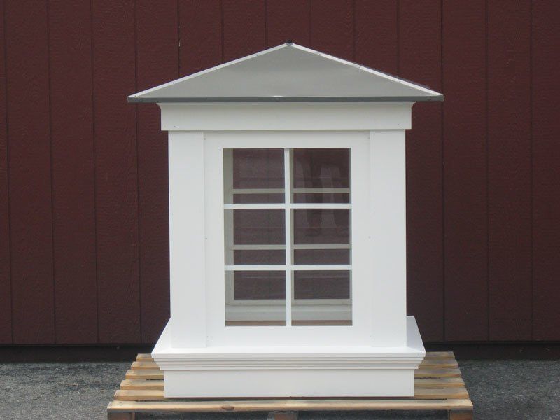 A white building with a roof and a window sits on a wooden pallet