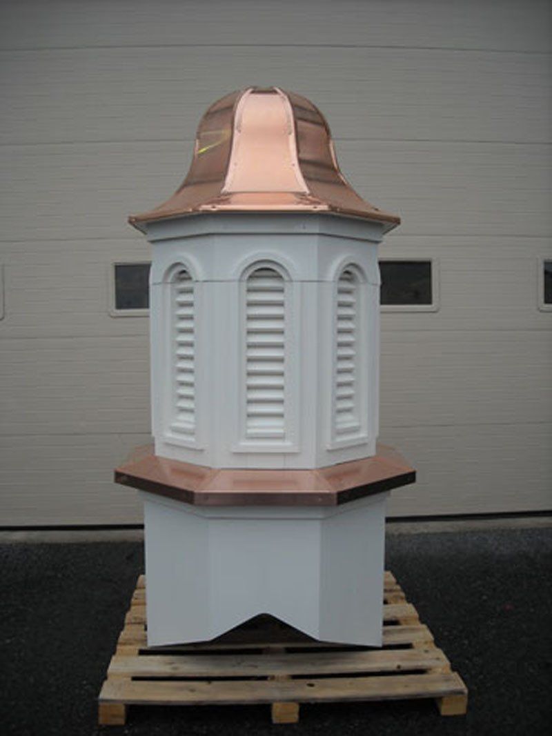 A white building with a copper roof is sitting on a wooden pallet.