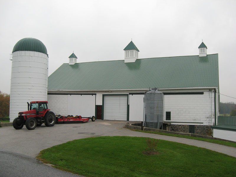 A red tractor is parked in front of a white barn with a green roof