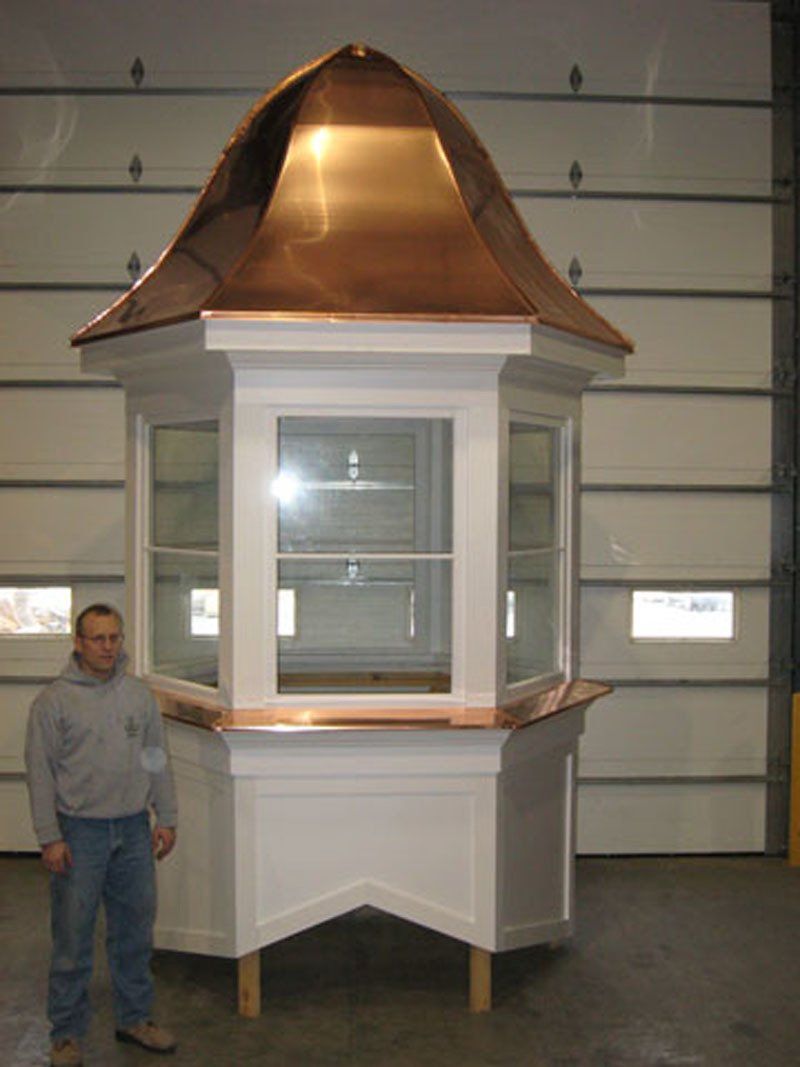 A man is standing next to a white building with a copper roof.