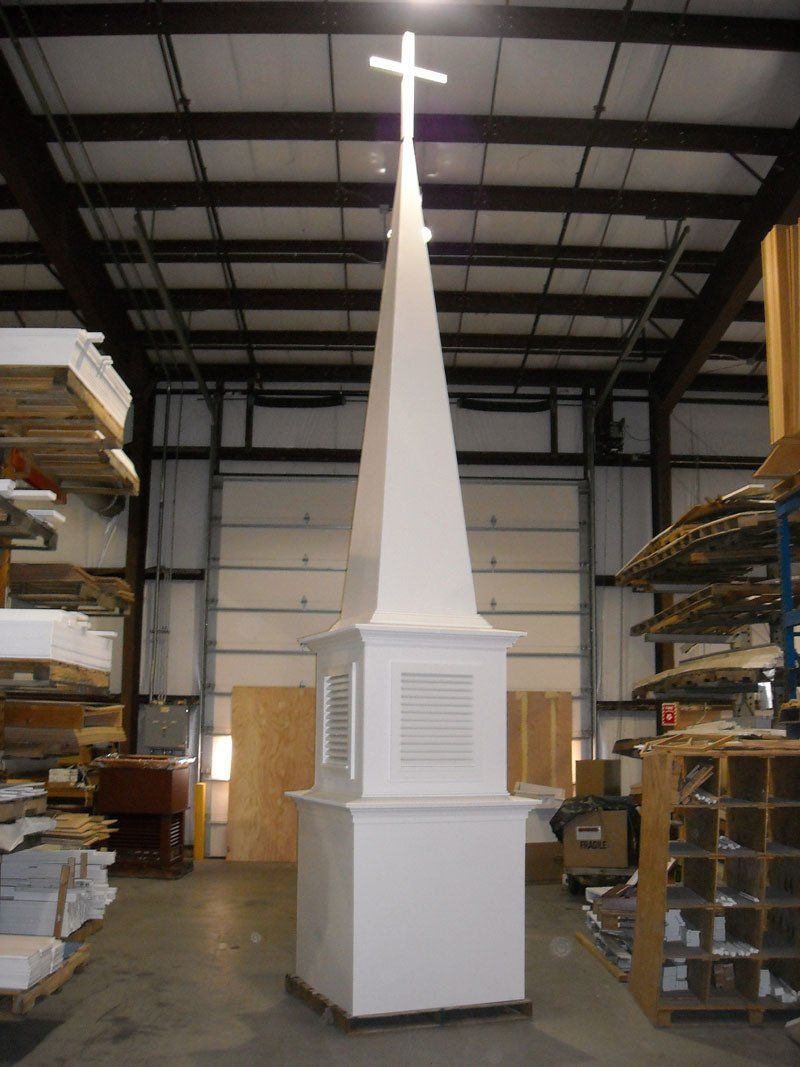 A large white obelisk with a cross on top in a warehouse