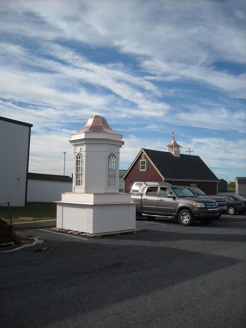 A statue in a parking lot with a red barn in the background