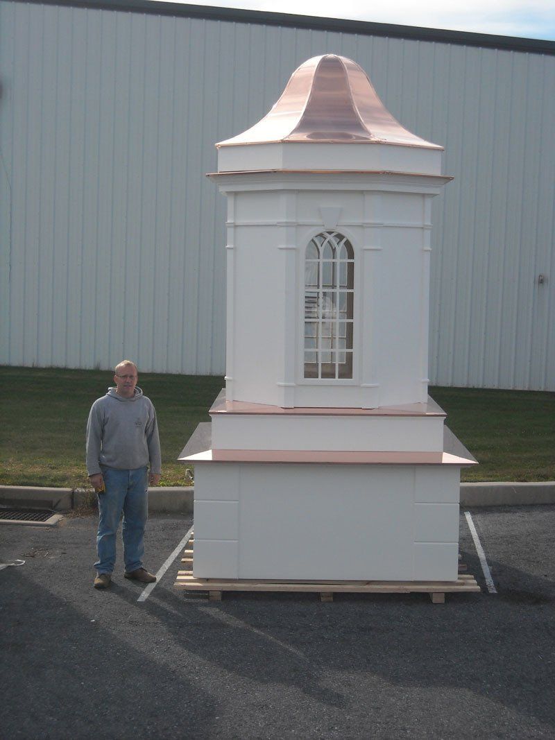 A man is standing next to a large white building with a copper roof.