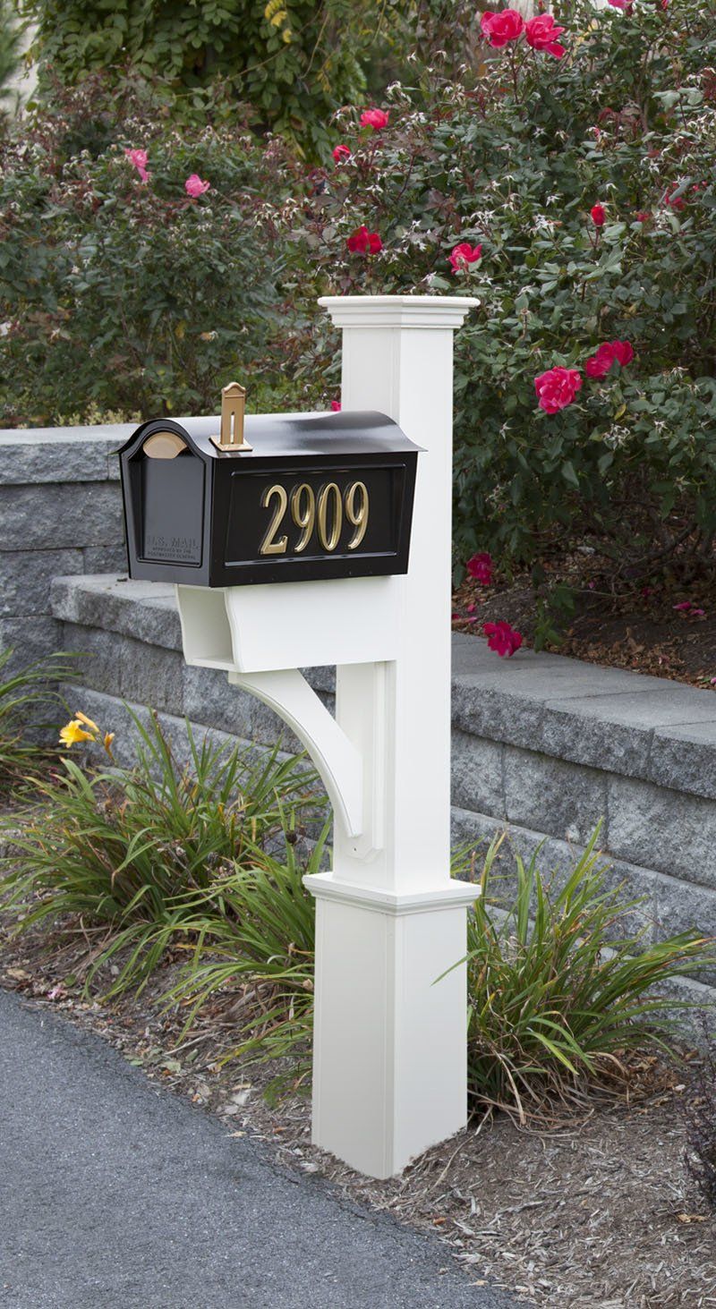A black mailbox is sitting on a white post next to a brick wall.