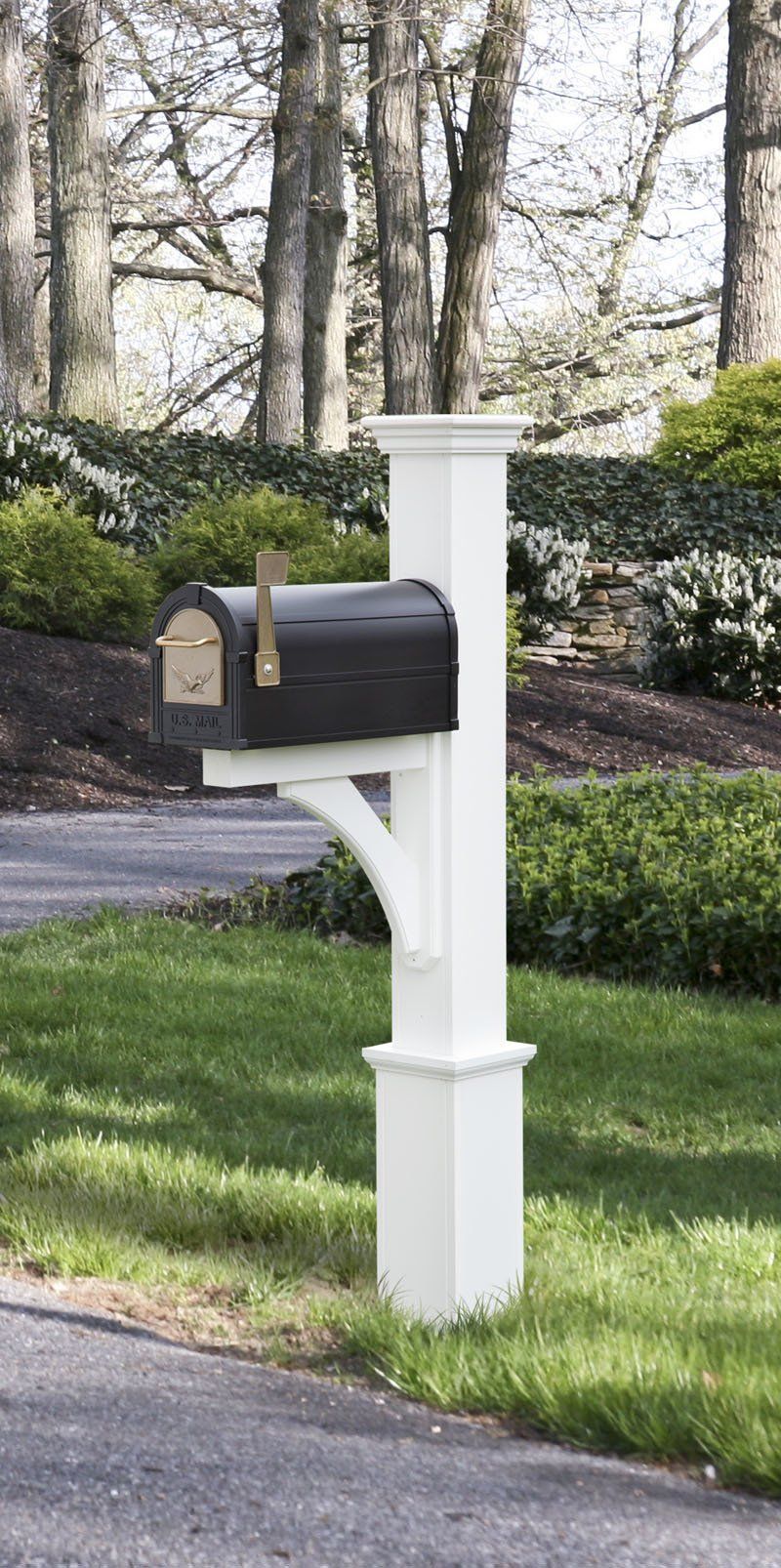 A black mailbox is sitting on a white post next to a driveway.