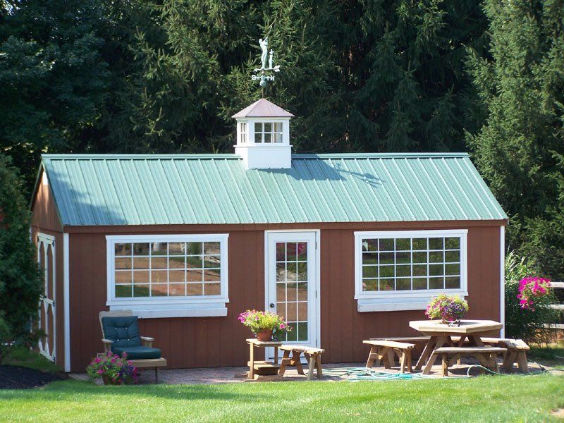 A brown shed with a green roof and a picnic table in front of it