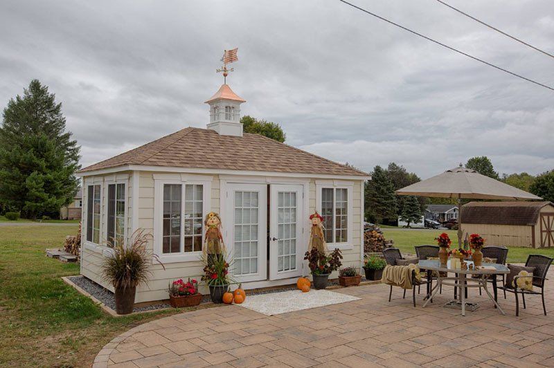 A small white house with a weather vane on top of it is sitting on top of a brick patio.