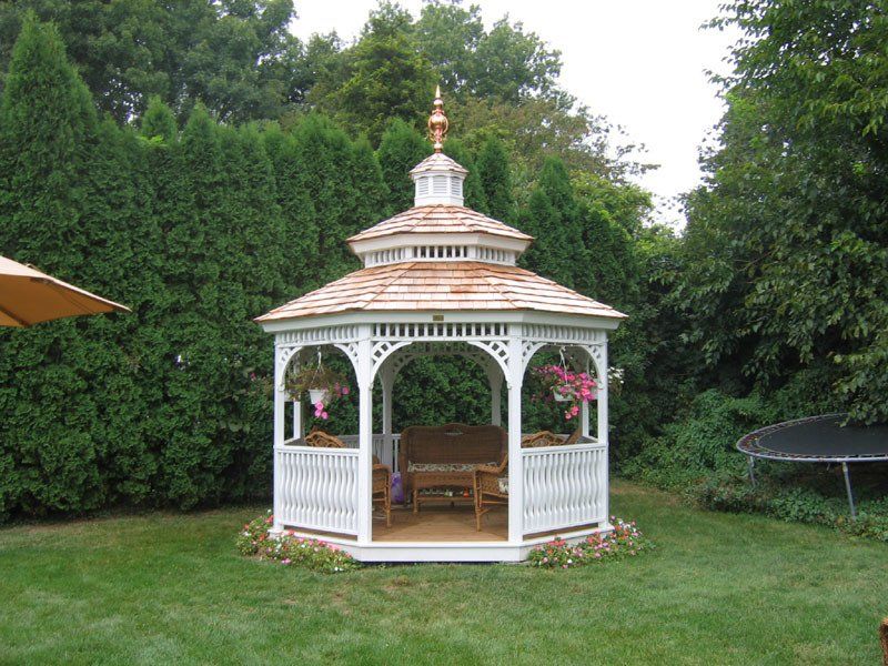 A white gazebo sits in the middle of a lush green backyard