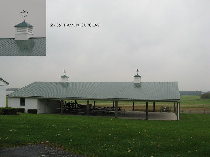 A picture of a barn with a green roof and two cupolas