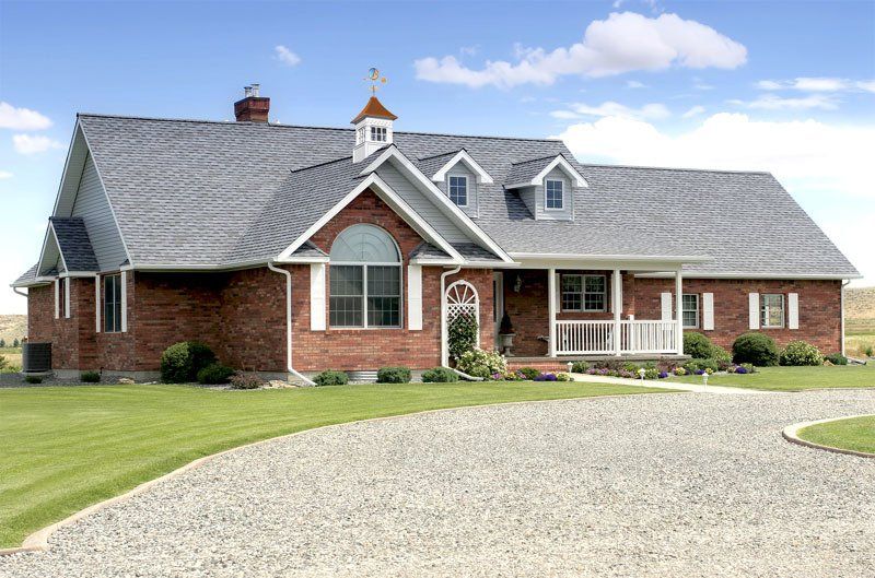 A large brick house with a gravel driveway in front of it