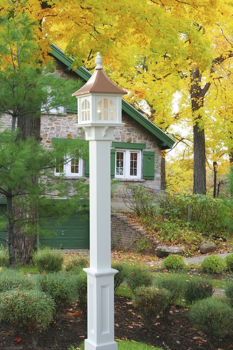 A white pole with a lamp on top of it in front of a house.