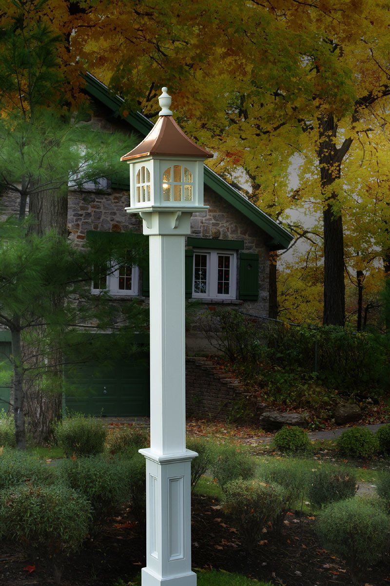 A white pole with a lantern on top of it in front of a house.