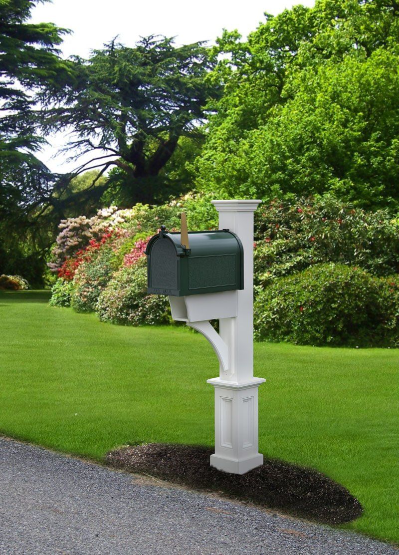 A green mailbox is sitting on a white post in the middle of a lush green field