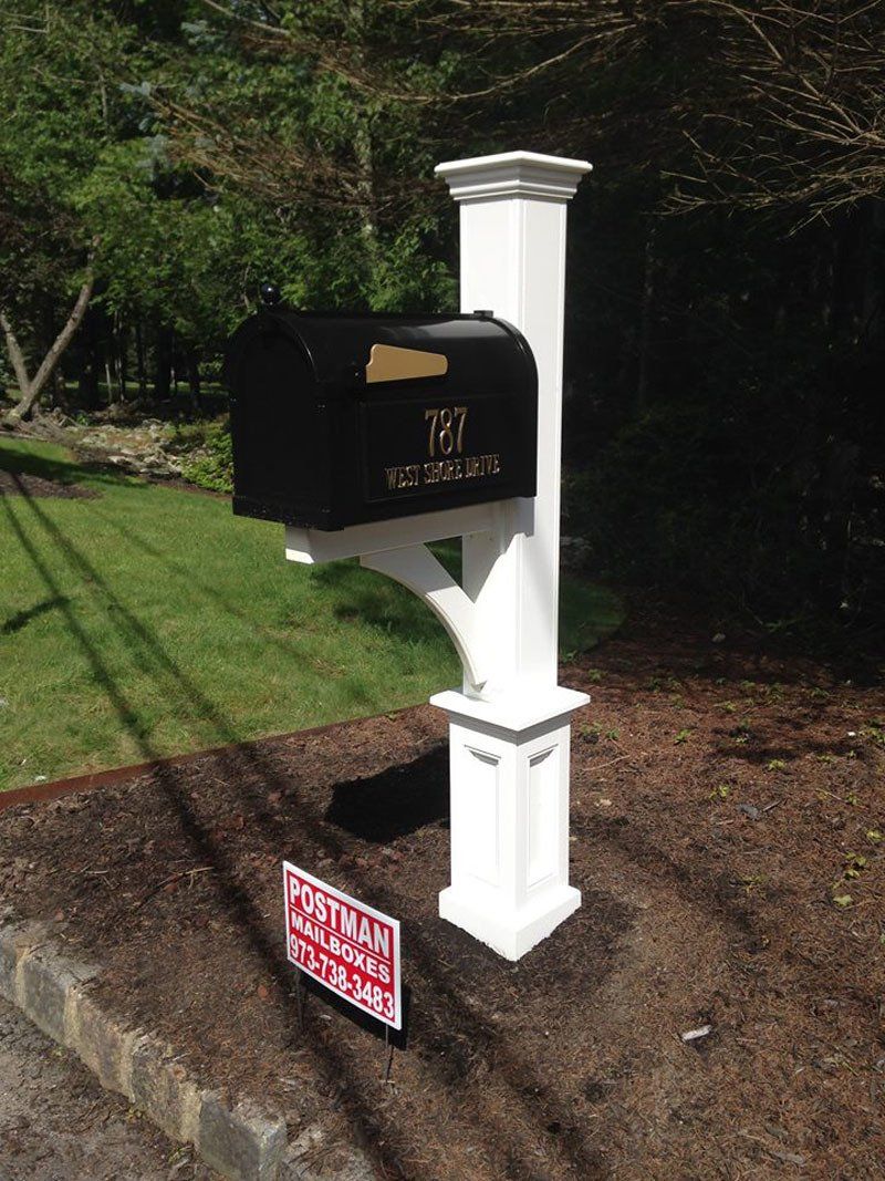A black mailbox is sitting on top of a white post.