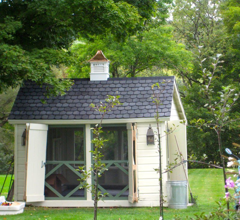 A small white house with a black roof is surrounded by trees