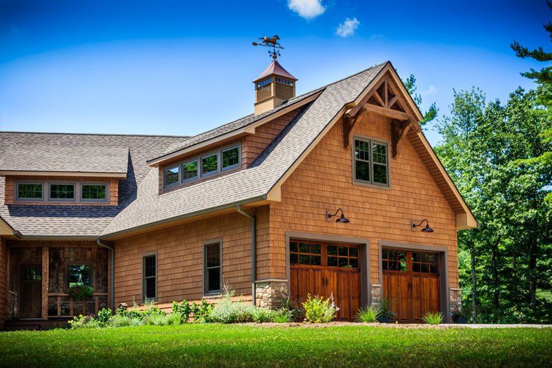 A large wooden house with two garage doors and a weather vane on the roof.