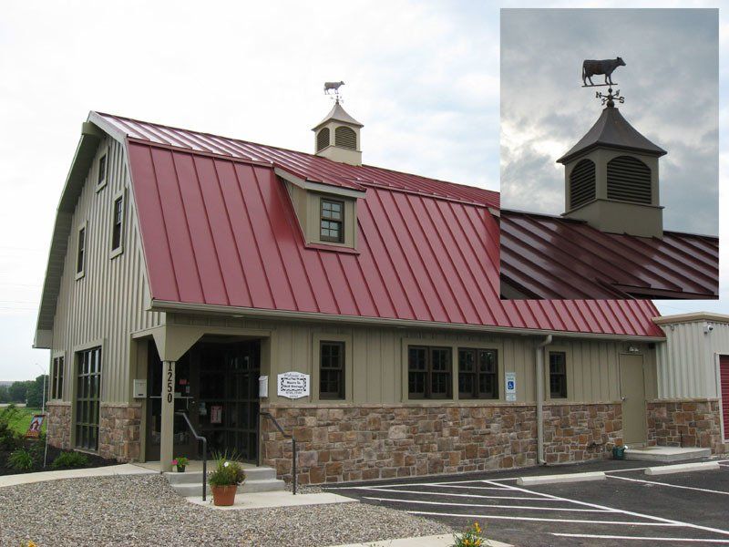 A barn with a red roof and a cow weather vane on top