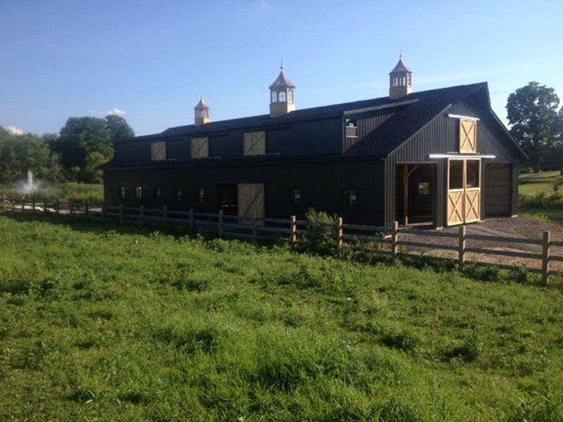 A large black barn is sitting in the middle of a grassy field.