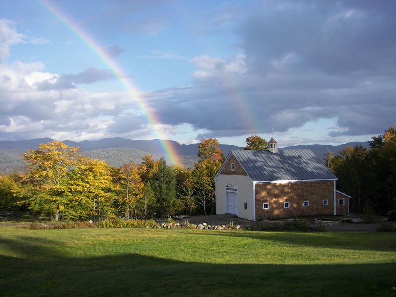 A rainbow is visible over a barn in a field.