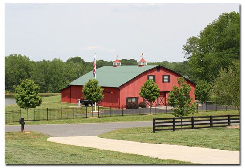 A red barn with a green roof is surrounded by trees and a fence