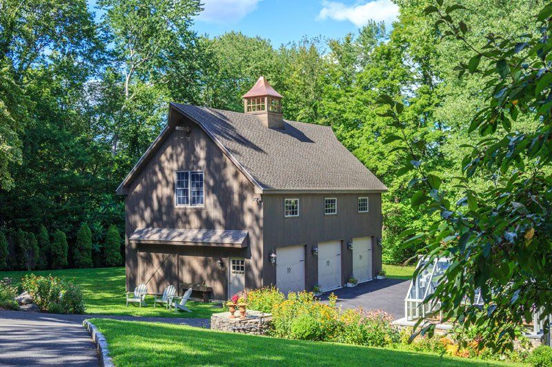 A large brown barn is sitting on top of a lush green hill surrounded by trees.